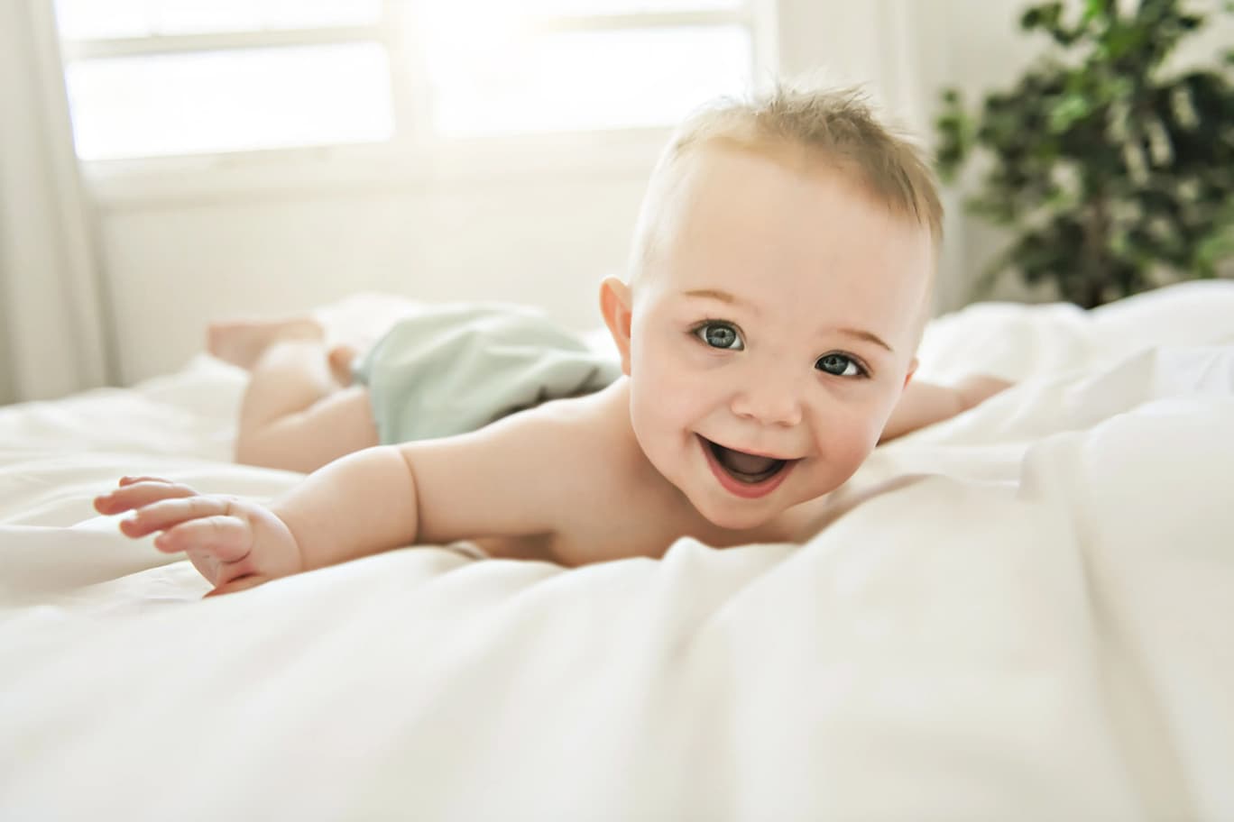 Baby liegt auf dem Bett und lacht in die Kamera.