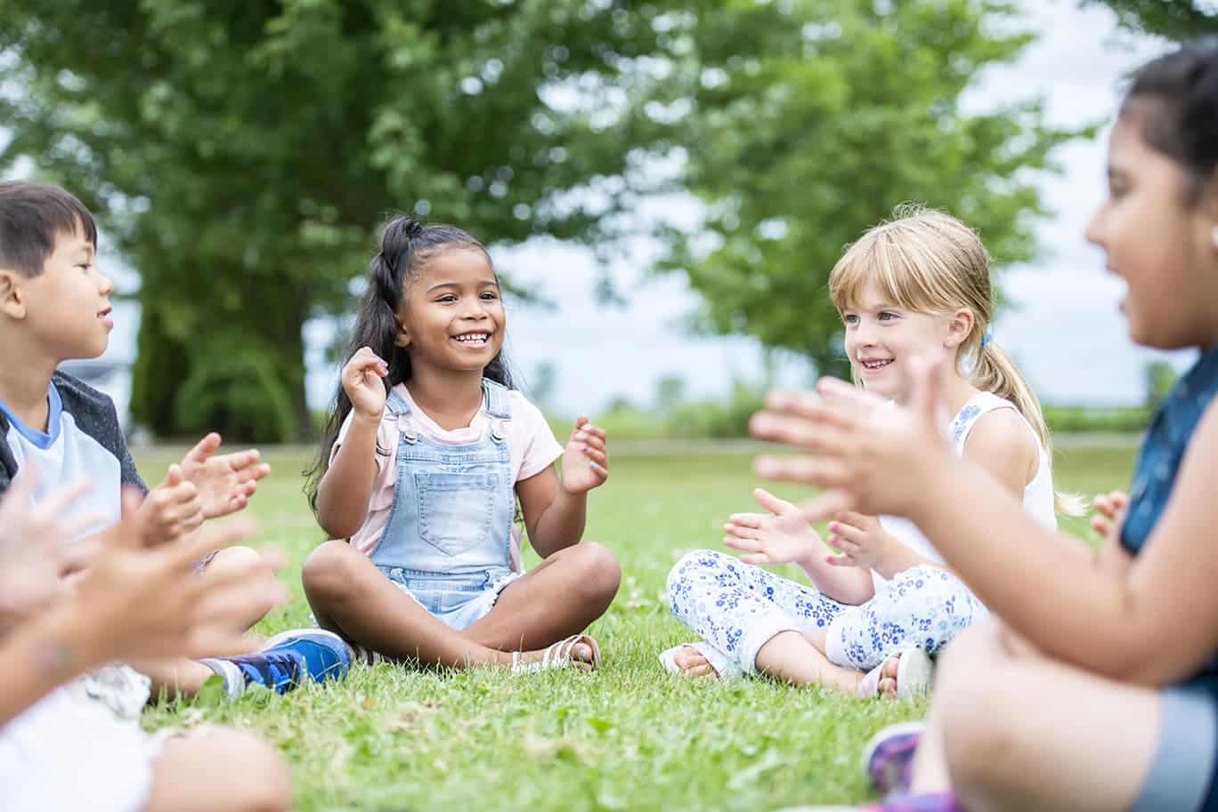 Kinder sitzen auf der Wiese im Kreis und klatschen und singen