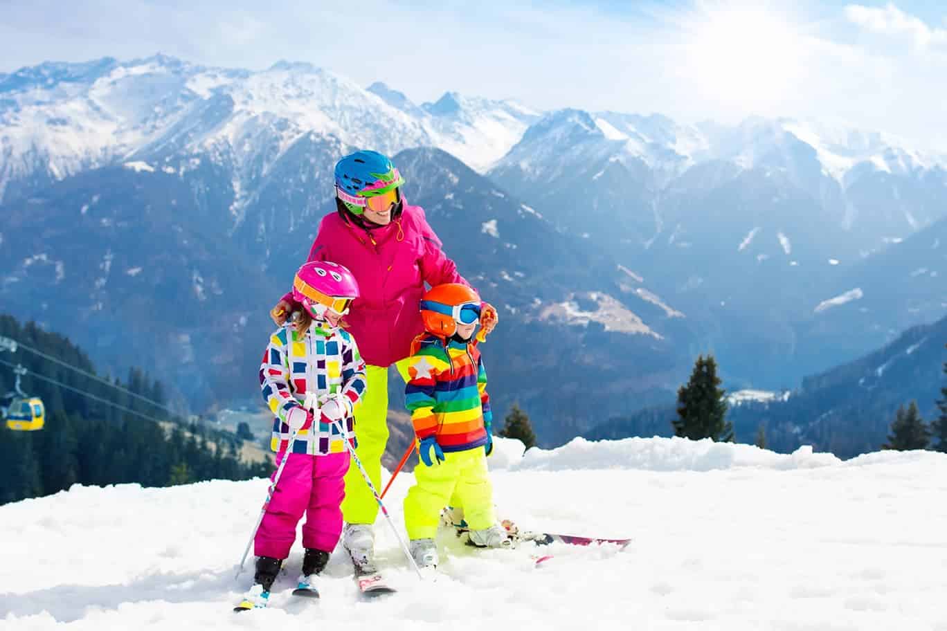 Skiferien mit der Familie, Kinder auf Skiern stehen mit Mama am Berg.
