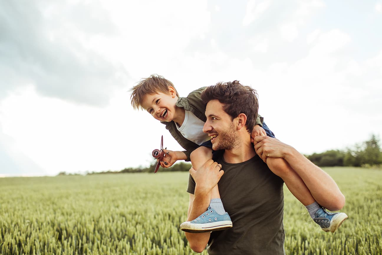 Vater mit Sohn auf den Schultern laufen durch Kornfeld