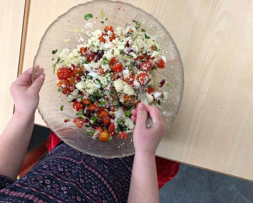 Kind würzt CousCous Salat in Glasschüssel