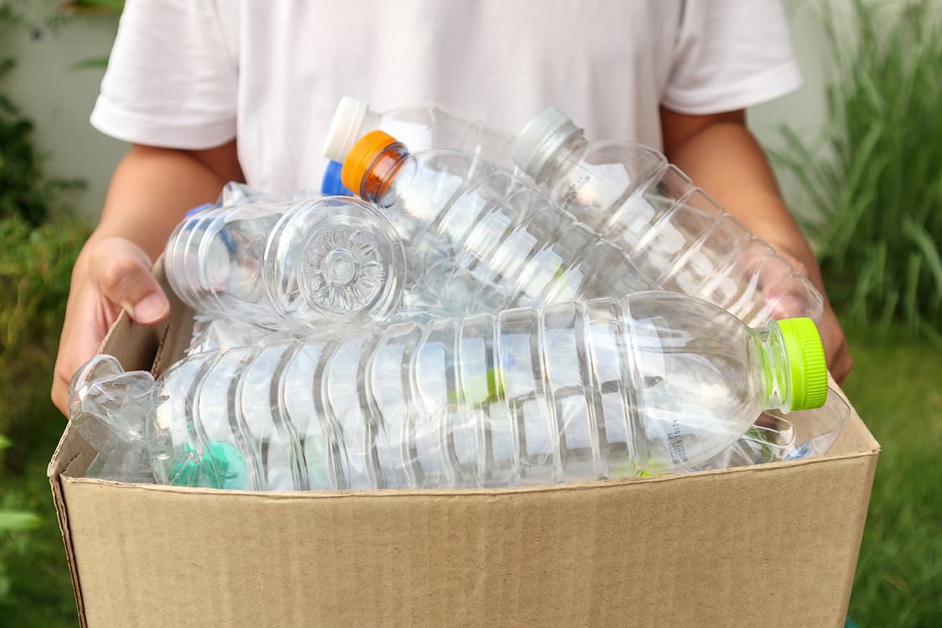 Kind sammelt Plastikflaschen in einem Karton.