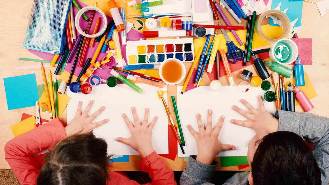 Kinder spielen an einem Tisch mit Malstiften und Wasserfarbe