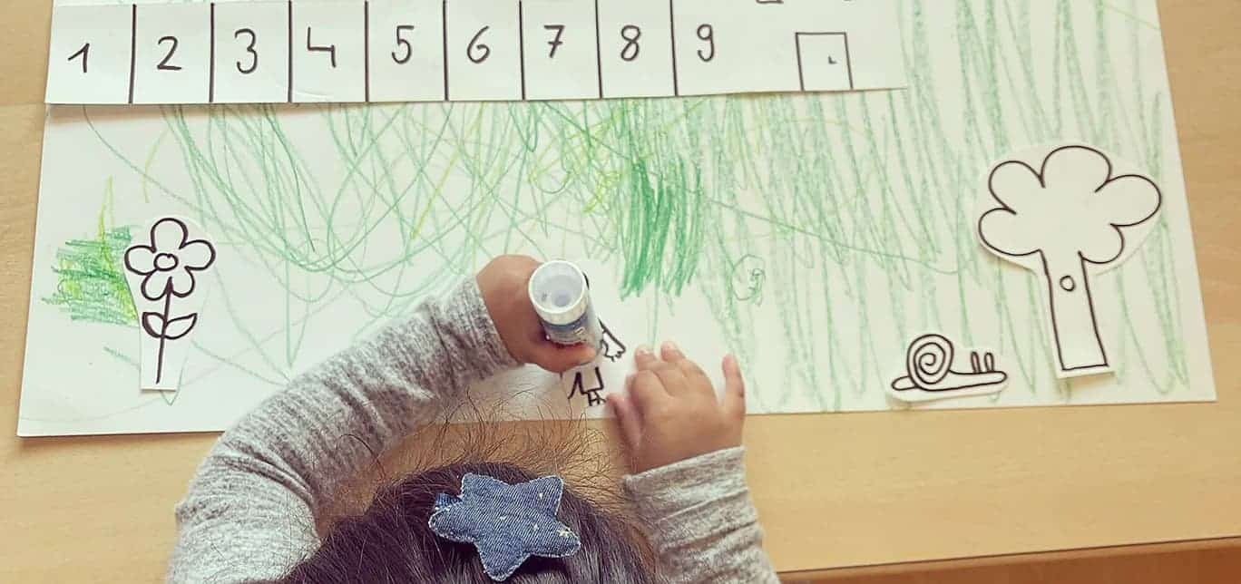 Kind bastelt Kalender an Tisch, mit Farben, Schere und Leimstift